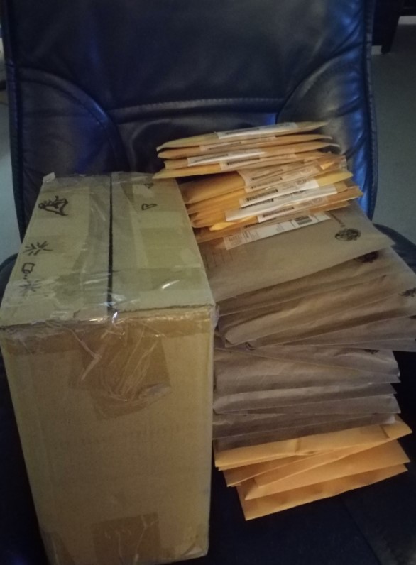 A tall stack of envelopes on a chair, sitting next to a taped-up cardboard box